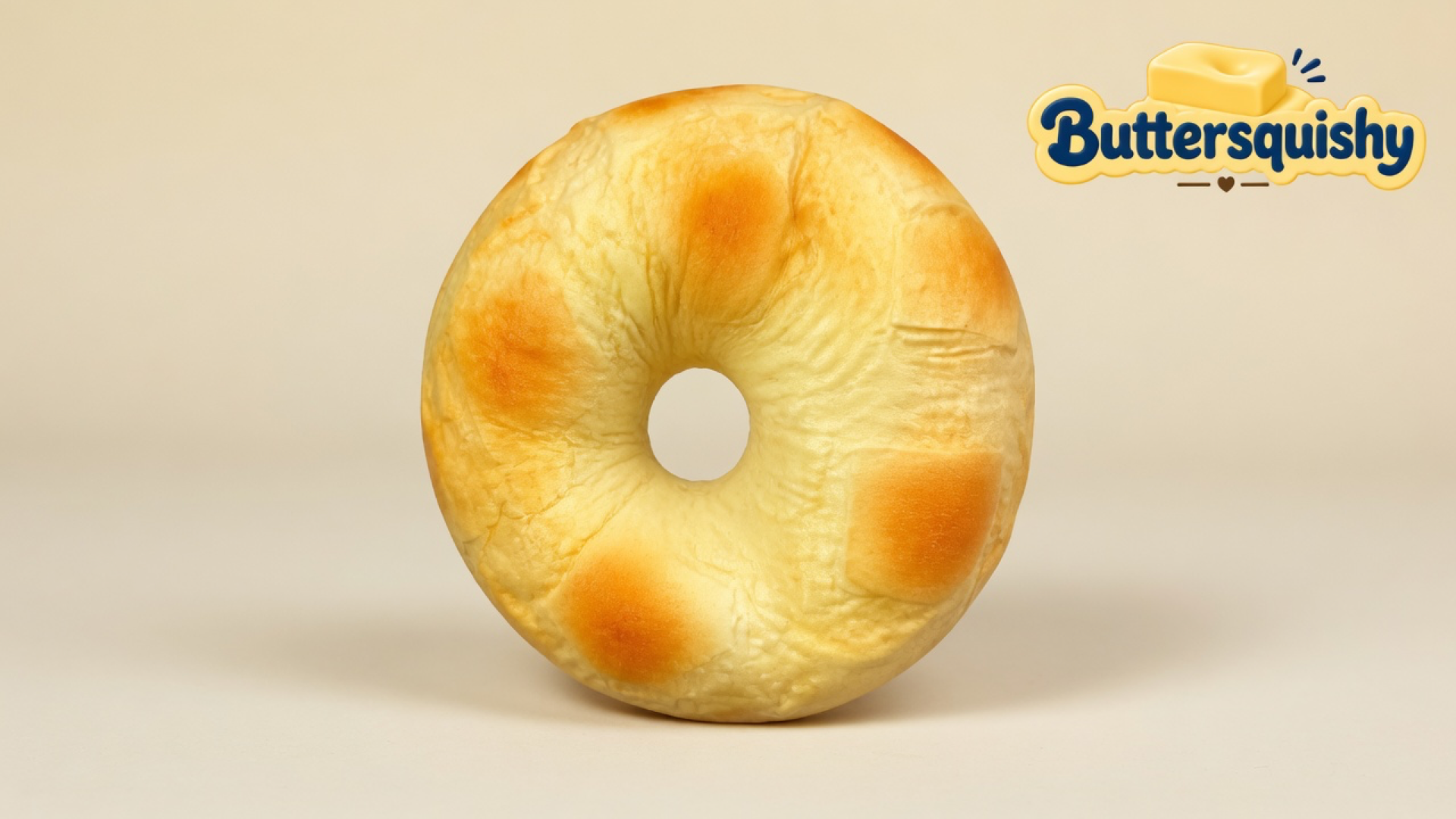 A single ring-shaped golden Bread Toast Loaf with toasted oval patches and an empty center hole on a light-yellow cream studio, Buttersquishy logo once at the upper right