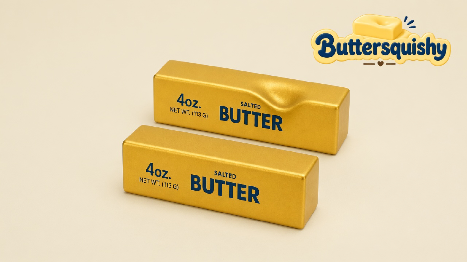 Two metallic gold-foil Golden Butter Stick loaves printed 4oz. NET WT. (113 G) SALTED BUTTER on a soft light-yellow cream studio surface, one with a thumb dent, Buttersquishy logo in the upper right