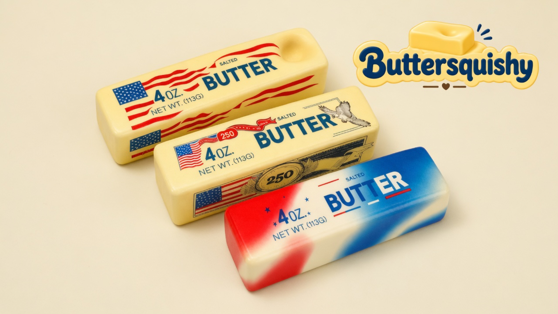 Three Stars and Stripes Butter sticks — two pale-yellow flag wrappers and one red-white-blue marble loaf — on a light cream studio surface, Buttersquishy logo at upper right