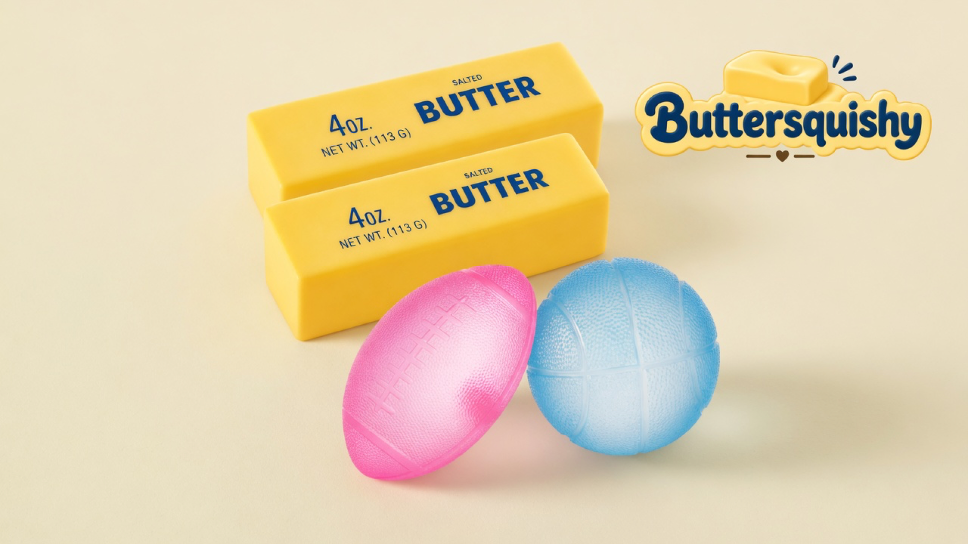 Two yellow salted-butter sticks stacked above a pink football and a light-blue basketball on a light-yellow cream studio, Buttersquishy logo at upper right