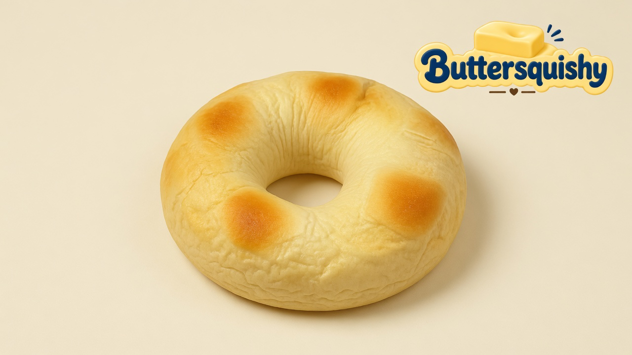 One pale milk-bread ring loaf with four golden toast patches and an open center hole on a light-yellow cream studio, Buttersquishy logo at upper right