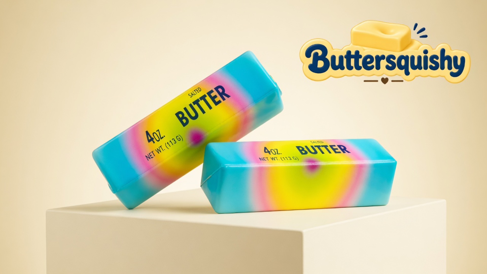 Two candy-melt butter sticks with cyan wraps, yellow fields, magenta hearts, and navy SALTED BUTTER type on a cream studio block, Buttersquishy logo in the upper right