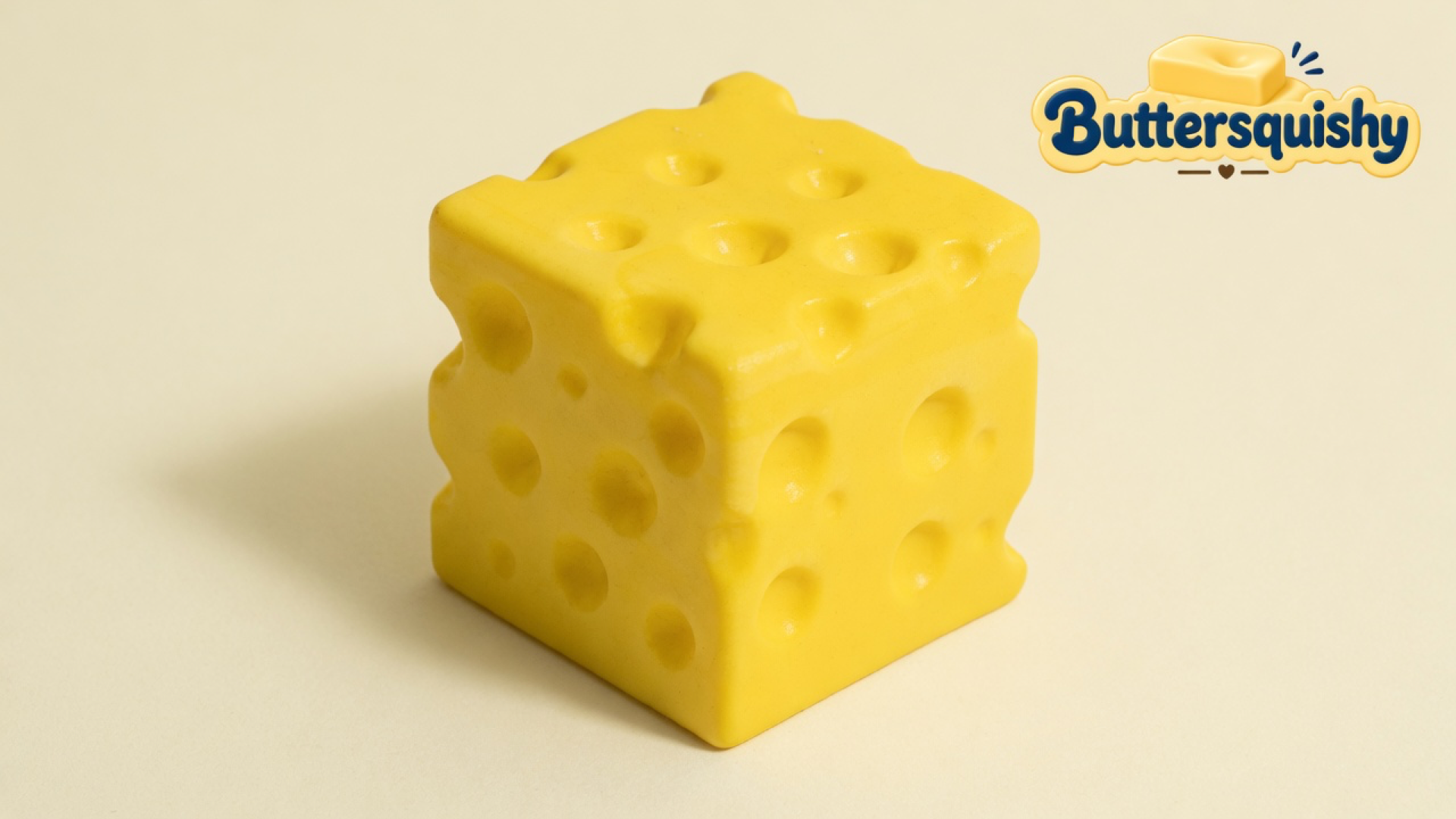 One yellow Swiss-hole Cheese Cube Loaf on a light-yellow cream studio surface, Buttersquishy logo in the upper right