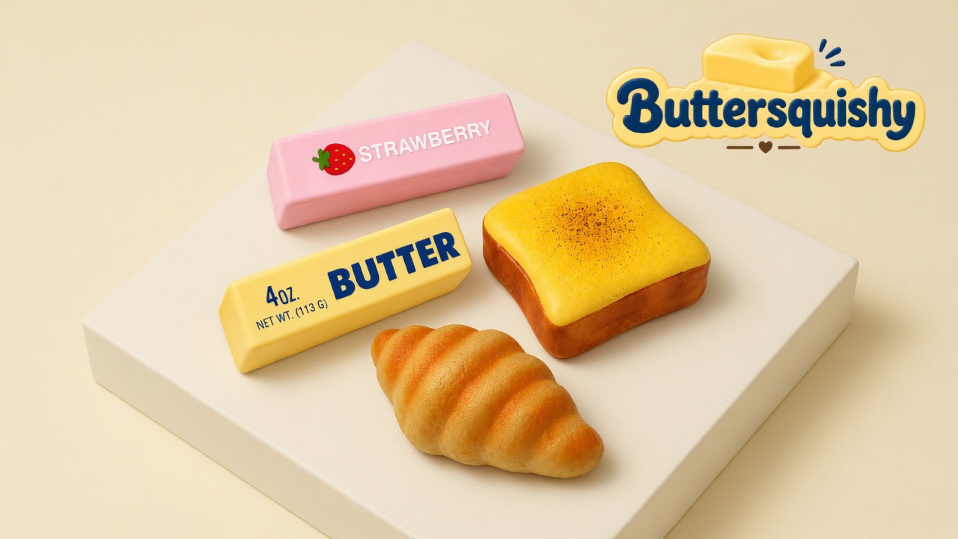Four bakery-skin toys — pink strawberry bar, yellow 4OZ. butter stick, toasted square, croissant — on a light-yellow cream studio, Buttersquishy logo at upper right