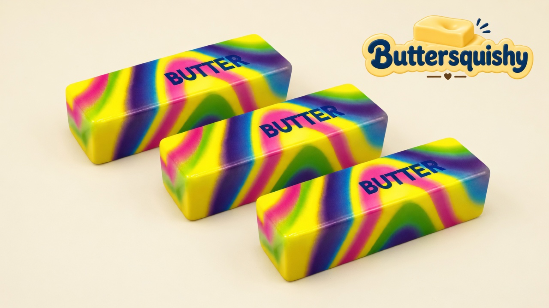 Three neon yellow-pink-purple-green swirl butter sticks printed BUTTER on a light-yellow cream studio table, Buttersquishy logo in the upper right