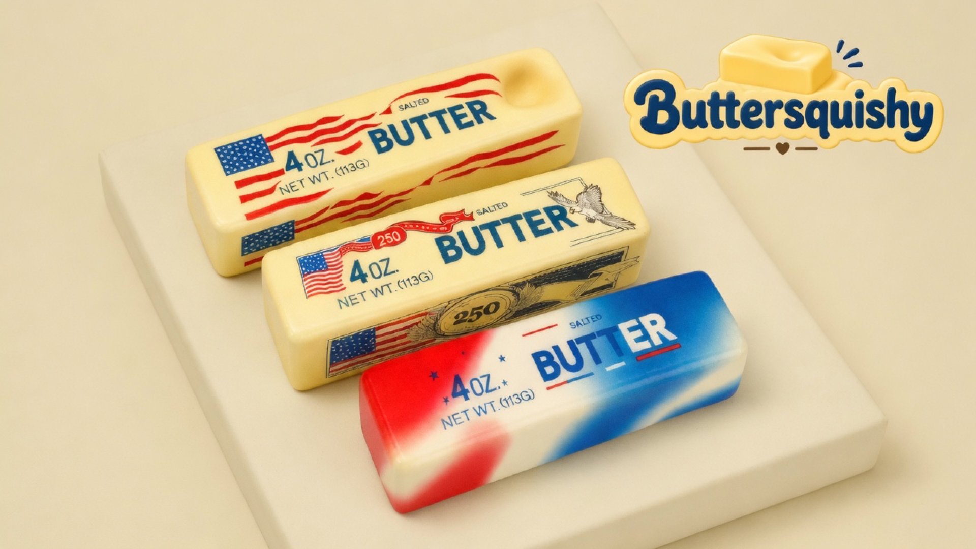 Three Stars and Stripes Butter sticks — two pale-yellow flag wrappers and one red-cream-blue marble loaf — on a light-yellow cream studio block, Buttersquishy logo in the upper right