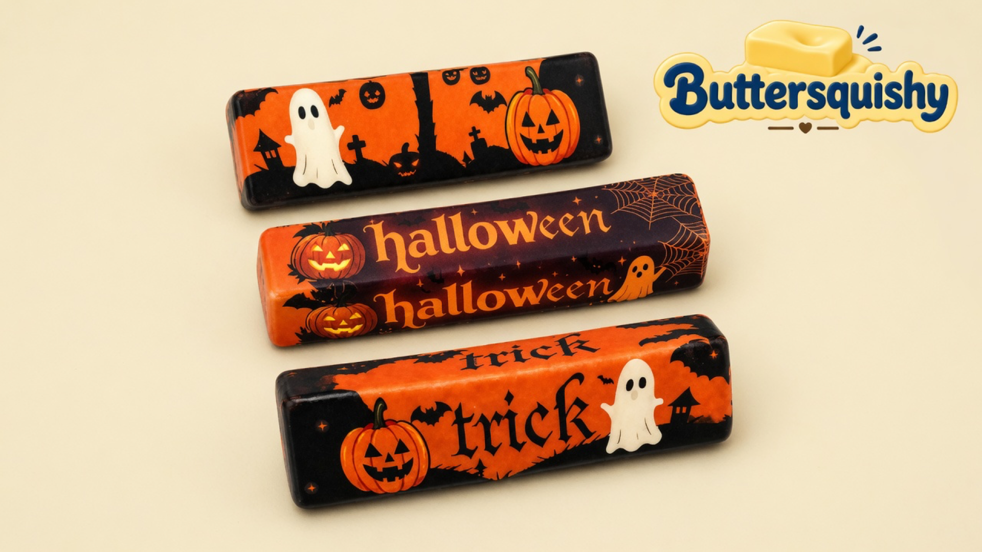 Three Halloween Ghost Butter sticks with ghost, pumpkin, halloween, and trick prints arranged as a gift trio on a cream studio surface, Buttersquishy logo in the upper right