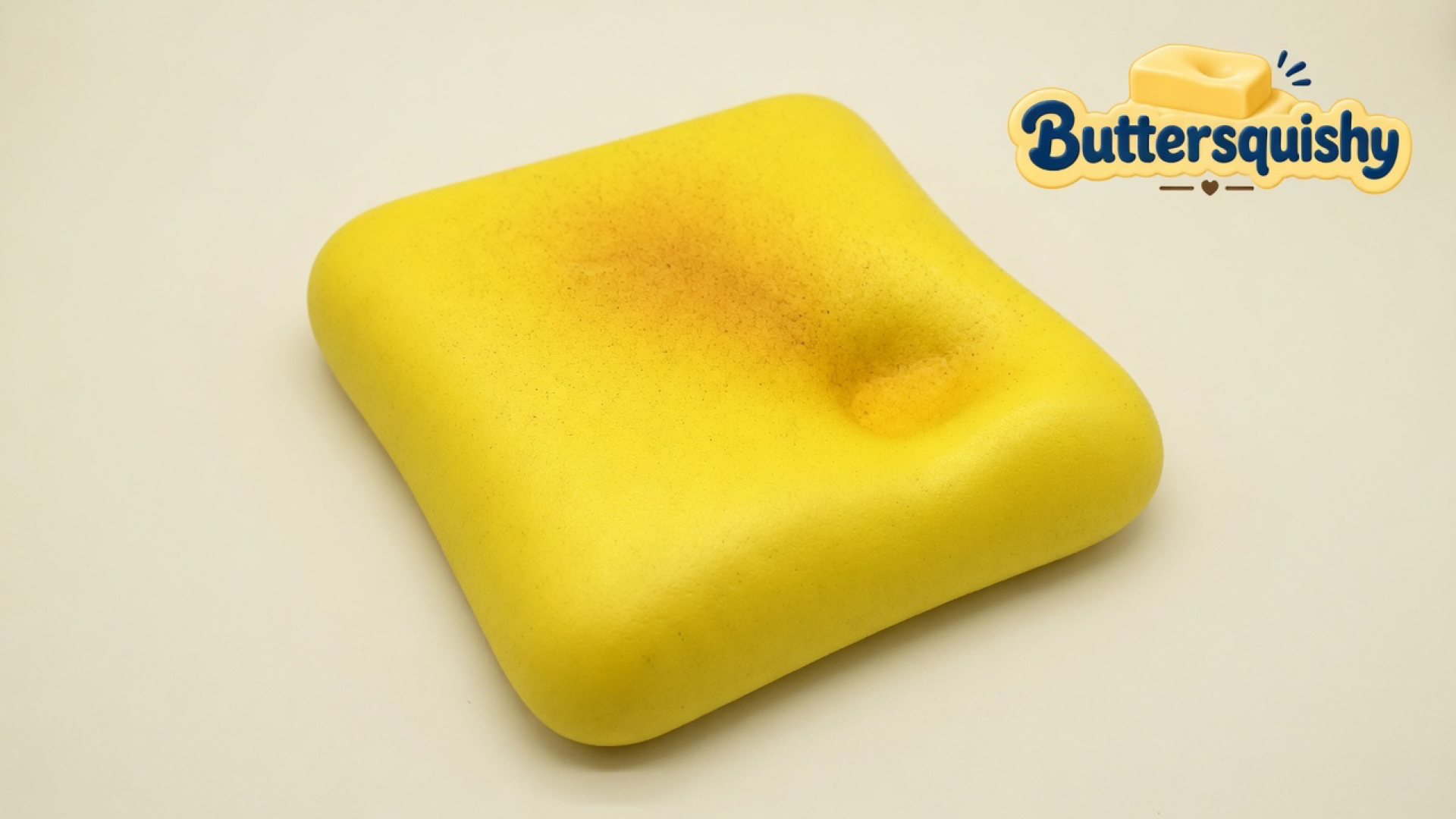 A yellow square Bread Toast Loaf with a toasted center and thumb dent on a light-yellow cream studio, Buttersquishy logo at upper right