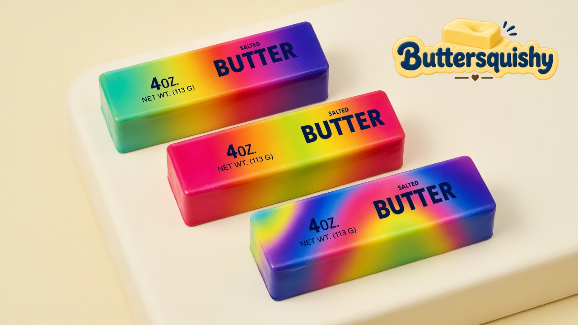 Three Candy Gradient Butter loaves — mint-to-violet, magenta with a lime wash, and an indigo swirl — printed with navy SALTED BUTTER type on a light-yellow cream studio table, Buttersquishy logo in the upper right