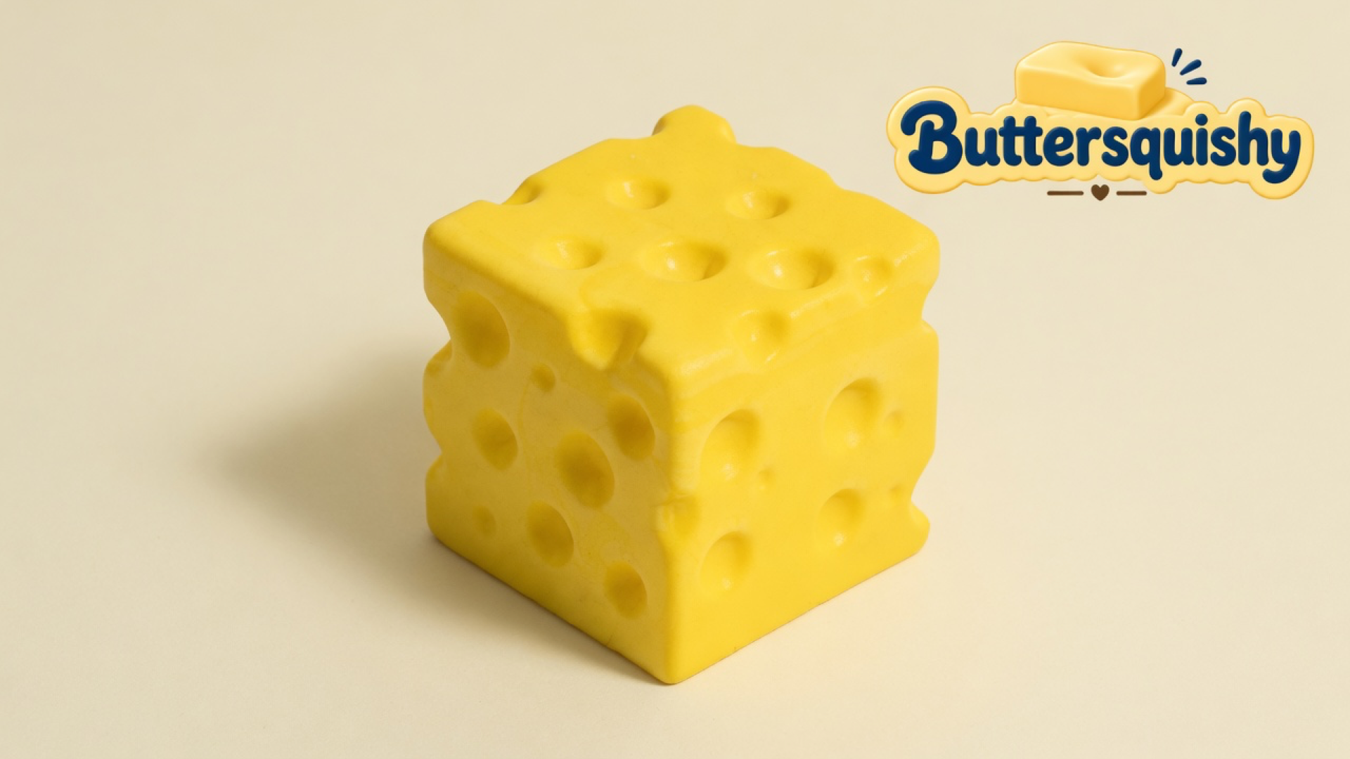 One cheddar-yellow holey Cheese Cube Loaf on a soft light-yellow cream studio surface, Buttersquishy logo in the upper right