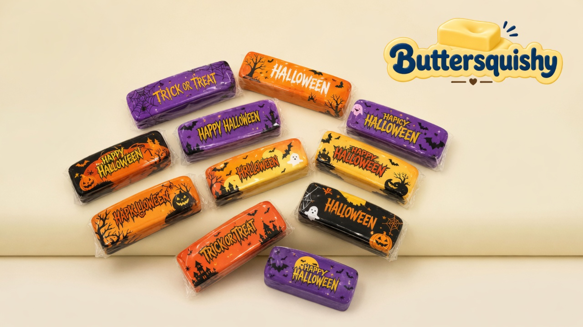 Twelve Halloween-print butter sticks in purple, orange, black, and yellow wraps on a light-yellow cream studio, Buttersquishy logo in the upper right