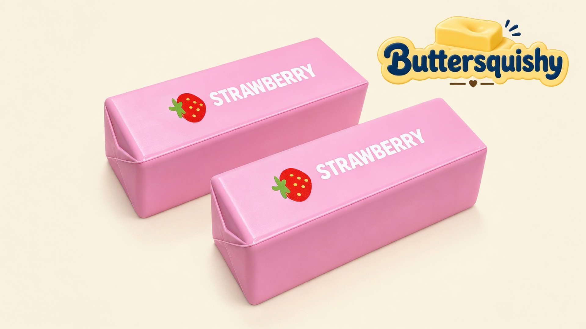 Two candy-pink strawberry butter-stick loaves printed STRAWBERRY with a cartoon berry, on a light-yellow cream studio, Buttersquishy logo in the upper right