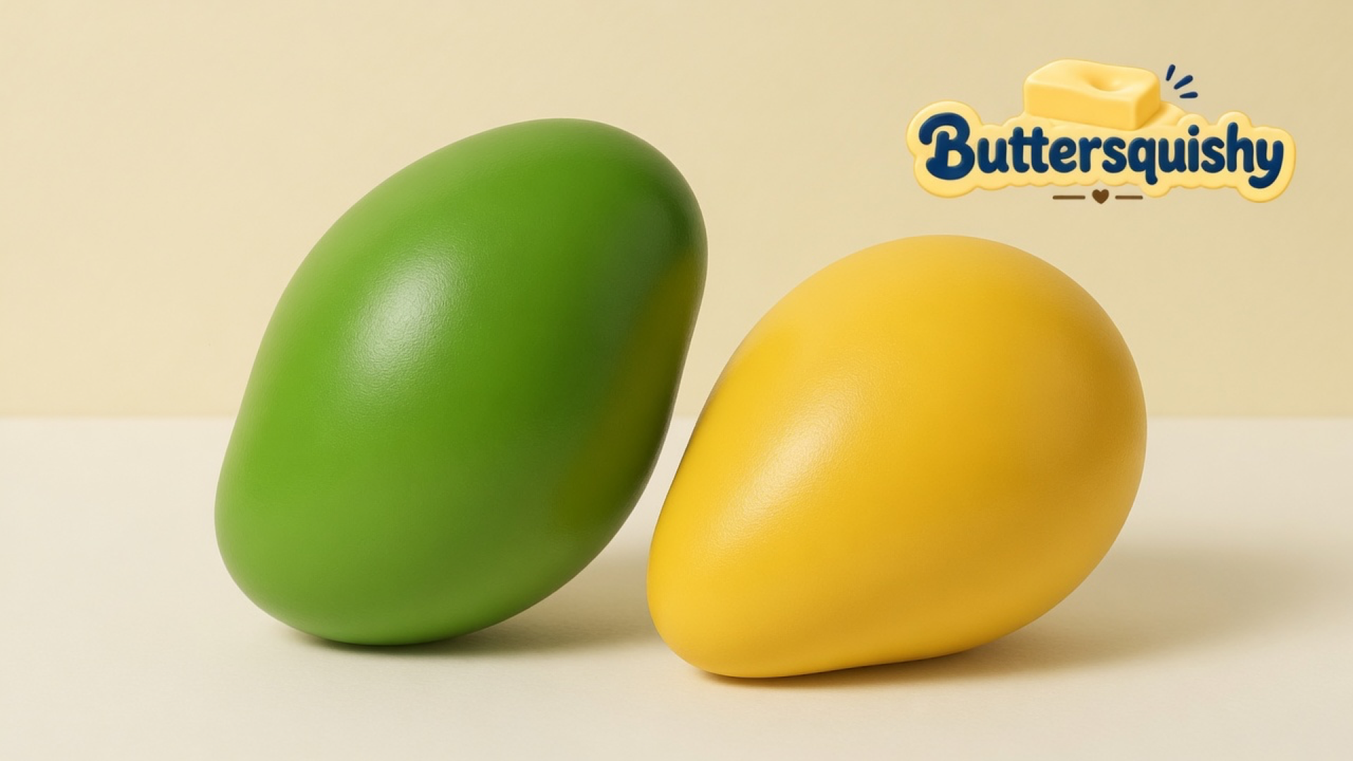 Green oval mango squishy and yellow teardrop mango squishy on a light-yellow cream studio table, Buttersquishy logo in the upper right