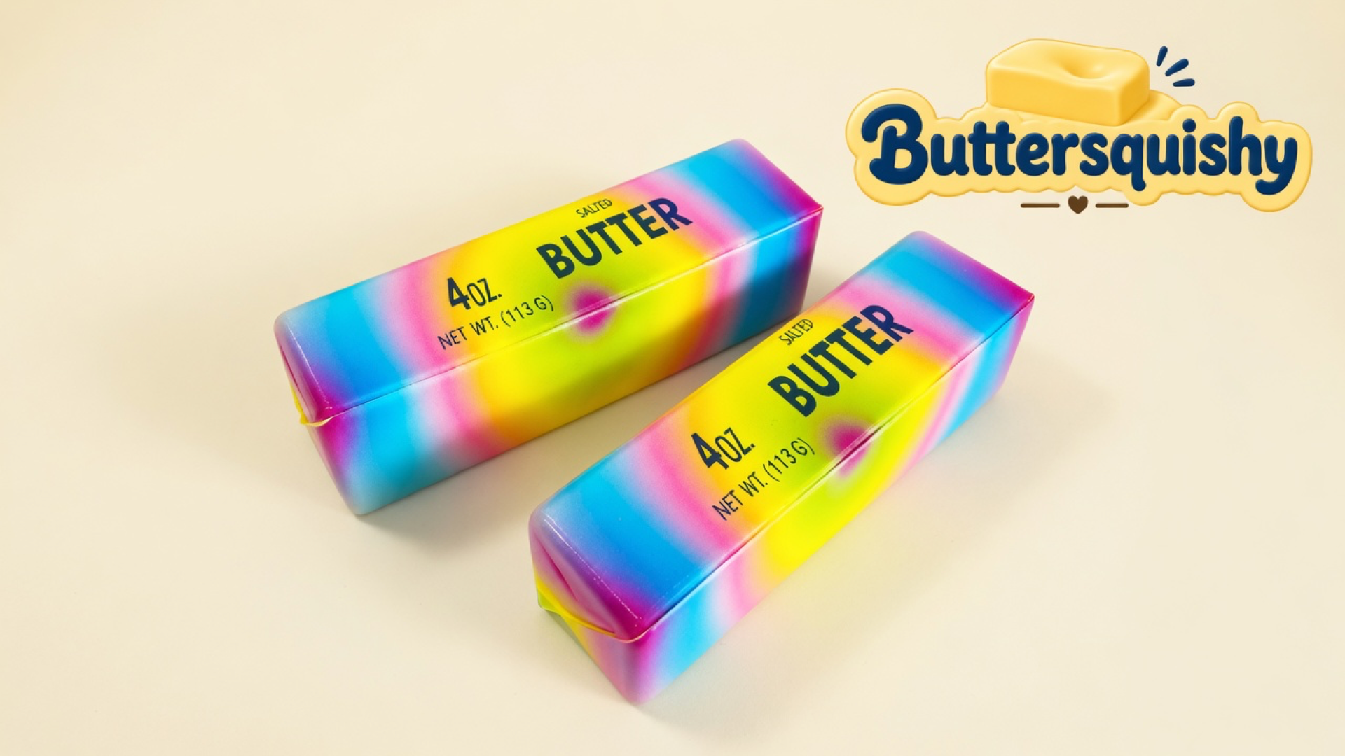 Two candy-rainbow butter sticks printed 4OZ. NET WT. (113 G) SALTED BUTTER on a light-yellow cream studio, Buttersquishy logo in the upper right
