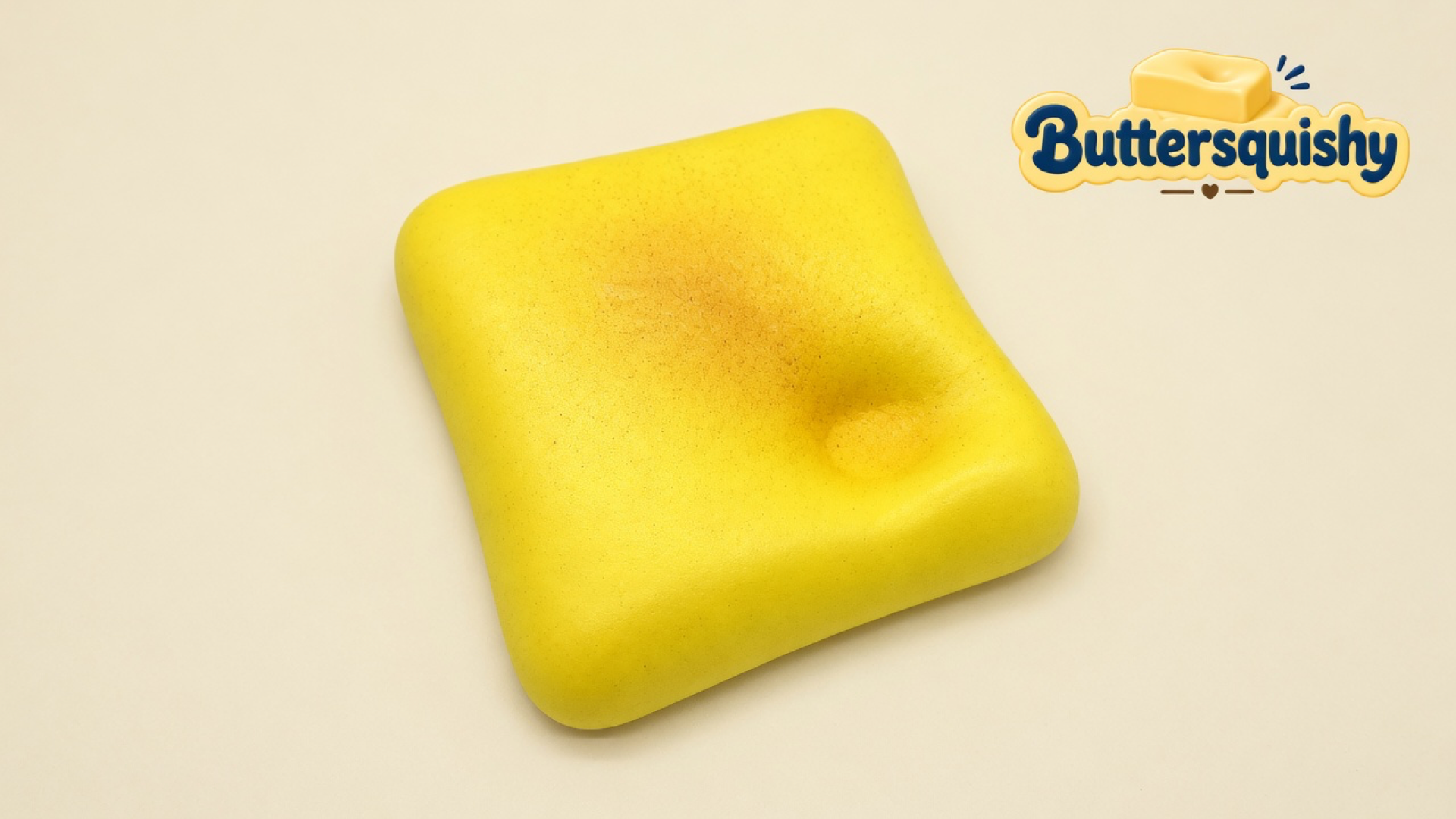 A square golden toast-face loaf with a toasted patch and a finger dent on a light-yellow cream studio, Buttersquishy logo in the upper right