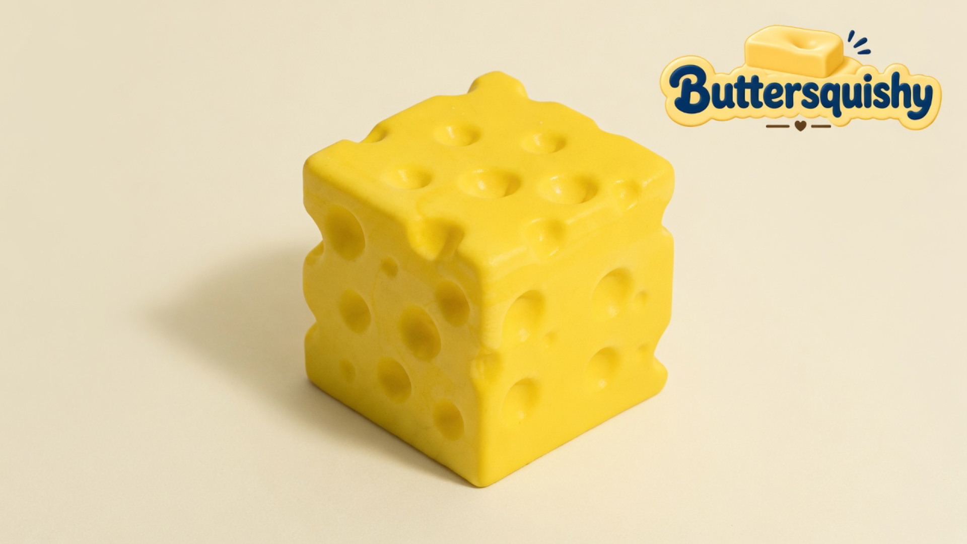 One yellow Cheese Cube Loaf with mixed-size Swiss holes on a light-yellow cream studio surface, Buttersquishy logo in the upper right