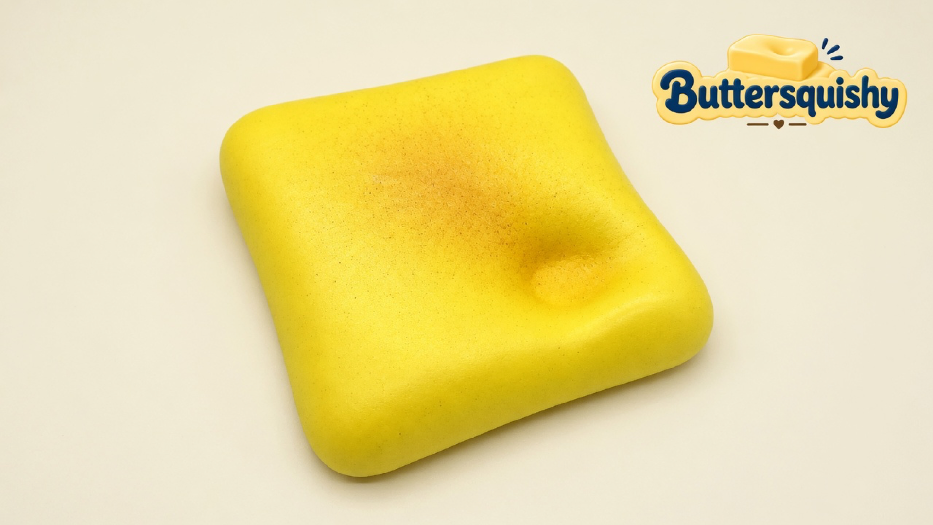One yellow square Bread Toast Loaf with a golden toasted center and a thumb dimple on a light-yellow cream studio surface, Buttersquishy logo in the upper right