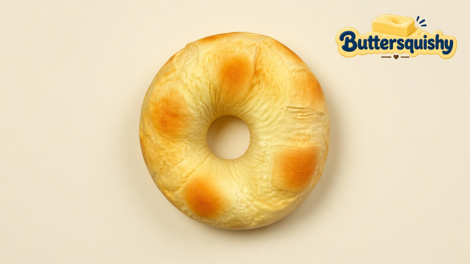 One toasted milk-bread ring loaf with four golden patches and a center hole on a light-yellow cream studio surface, Buttersquishy logo in the upper right