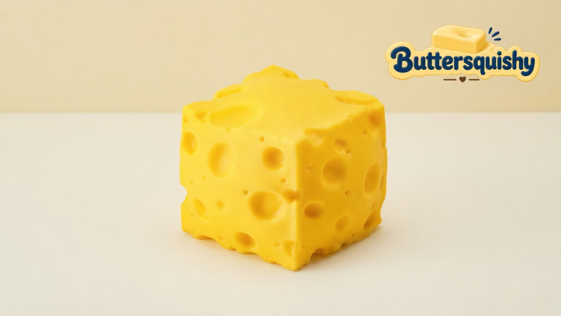 One yellow Cheese Cube Loaf cube with mixed-size holes on a light-yellow cream studio surface, Buttersquishy logo in the upper right